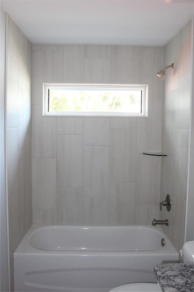 bathroom featuring tiled shower / bath combo, toilet, and a wealth of natural light