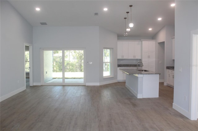 kitchen featuring sink, hanging light fixtures, a towering ceiling, a center island with sink, and white cabinets