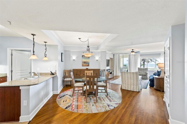 dining space with ceiling fan, a raised ceiling, hardwood / wood-style floors, and sink