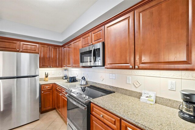 kitchen with light stone counters, appliances with stainless steel finishes, light tile patterned floors, and tasteful backsplash