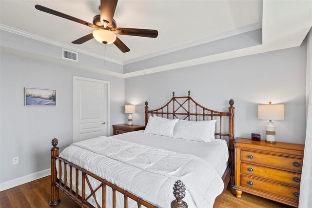 bedroom featuring crown molding, a tray ceiling, dark hardwood / wood-style floors, and ceiling fan