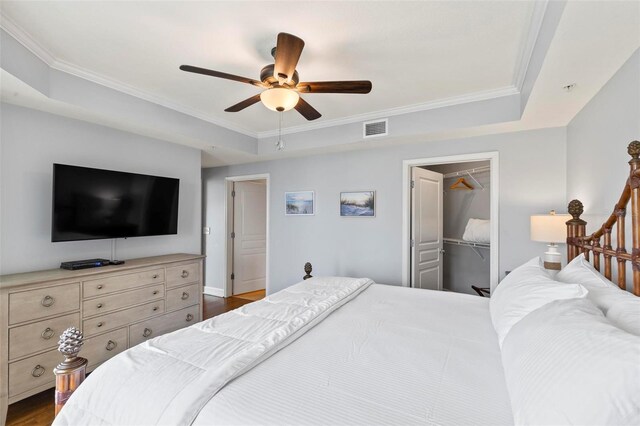 bedroom featuring a closet, dark hardwood / wood-style floors, a raised ceiling, a walk in closet, and ceiling fan