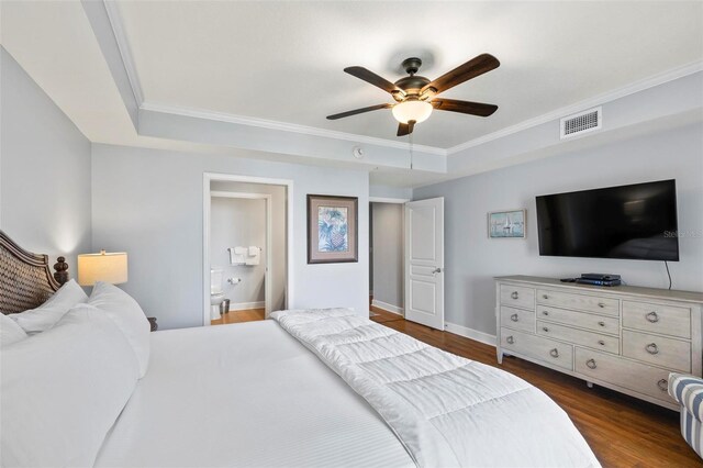 bedroom with ceiling fan, a tray ceiling, connected bathroom, and dark wood-type flooring