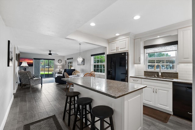 kitchen with dark hardwood / wood-style floors, a breakfast bar area, sink, black appliances, and white cabinetry