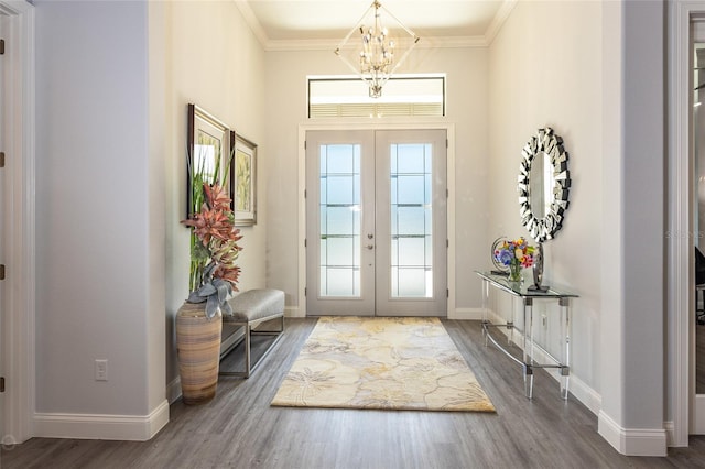 foyer entrance with french doors, wood-type flooring, ornamental molding, and a chandelier