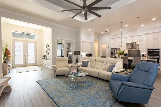 living room featuring light hardwood / wood-style floors, french doors, ornamental molding, and ceiling fan with notable chandelier