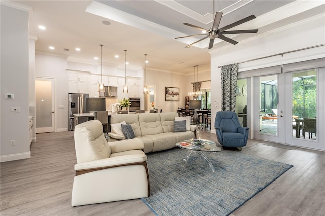 living room with ornamental molding, light wood-type flooring, and ceiling fan with notable chandelier