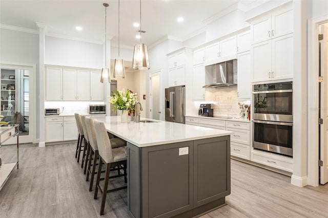 kitchen with wall chimney exhaust hood, appliances with stainless steel finishes, white cabinetry, and a center island with sink