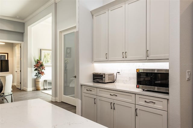 interior space featuring crown molding, light stone countertops, light hardwood / wood-style flooring, and white cabinets