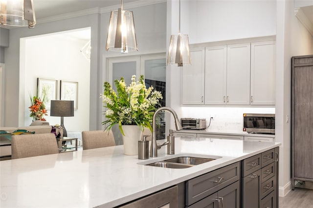 kitchen with hanging light fixtures, light stone countertops, light hardwood / wood-style floors, crown molding, and sink