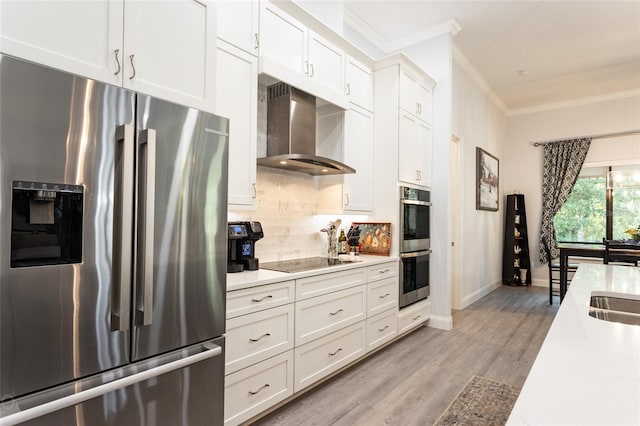 kitchen with wall chimney range hood, appliances with stainless steel finishes, light hardwood / wood-style floors, white cabinets, and ornamental molding