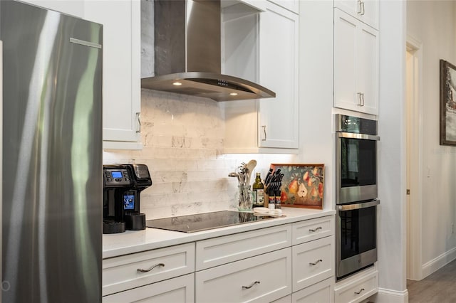 kitchen with decorative backsplash, hardwood / wood-style flooring, wall chimney exhaust hood, white cabinetry, and appliances with stainless steel finishes