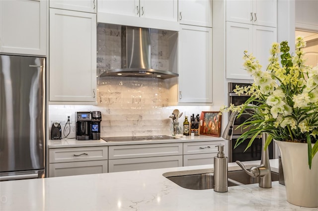 kitchen with wall chimney exhaust hood, stainless steel fridge, tasteful backsplash, white cabinetry, and black electric stovetop