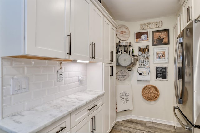 kitchen with stainless steel refrigerator, white cabinetry, light hardwood / wood-style flooring, and light stone counters