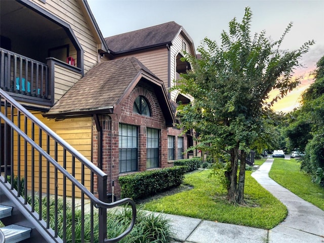 property exterior at dusk with a balcony and a lawn