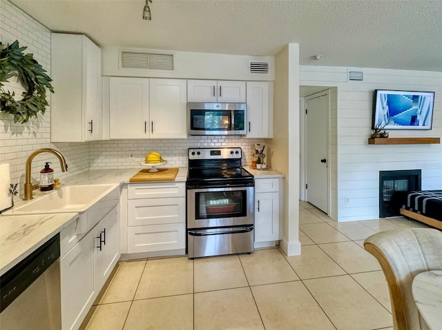 kitchen featuring sink, white cabinetry, decorative backsplash, wooden walls, and appliances with stainless steel finishes