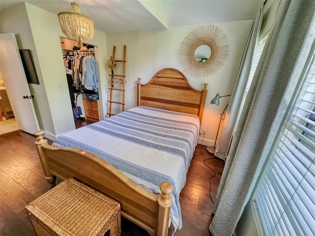 bedroom with a closet, a textured ceiling, dark wood-type flooring, a notable chandelier, and a spacious closet