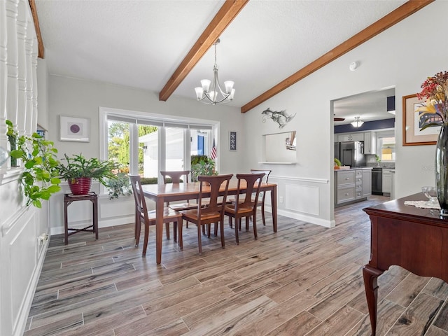 dining space featuring ceiling fan with notable chandelier, light hardwood / wood-style flooring, and lofted ceiling with beams