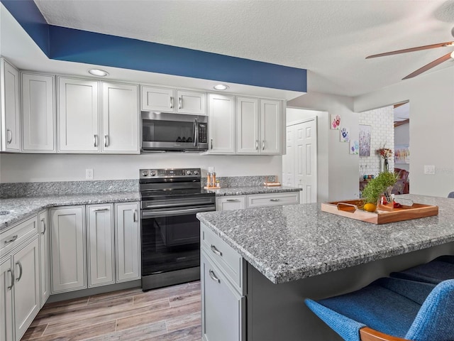 kitchen featuring light hardwood / wood-style floors, a textured ceiling, a kitchen bar, appliances with stainless steel finishes, and ceiling fan