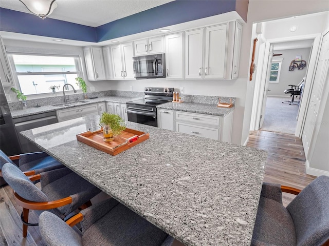 kitchen featuring light wood-type flooring, sink, white cabinets, a kitchen bar, and appliances with stainless steel finishes