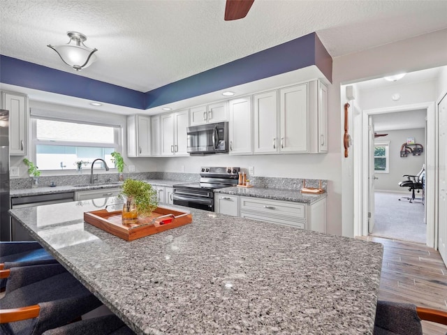 kitchen with appliances with stainless steel finishes, light stone counters, a breakfast bar, a textured ceiling, and wood-type flooring