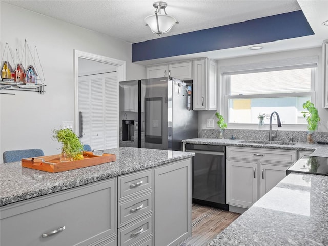 kitchen with light wood-type flooring, sink, a textured ceiling, stainless steel appliances, and light stone countertops