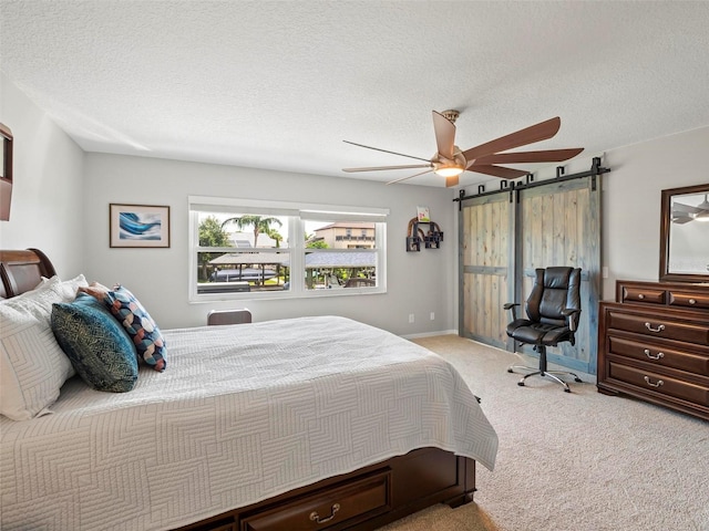 bedroom with light carpet, a textured ceiling, ceiling fan, and a barn door