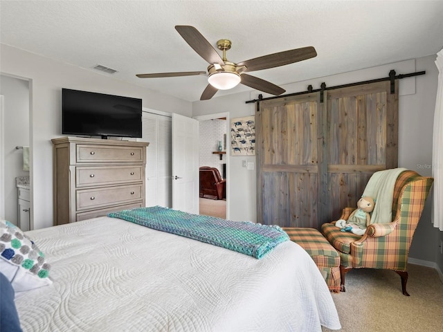 bedroom with a closet, a textured ceiling, carpet floors, a barn door, and ceiling fan