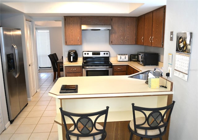 kitchen with kitchen peninsula, appliances with stainless steel finishes, sink, light tile patterned floors, and a breakfast bar area