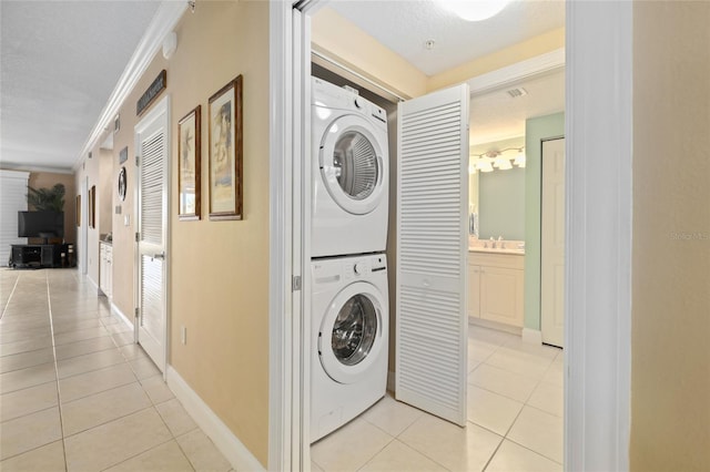 laundry room with light tile patterned floors, sink, a textured ceiling, crown molding, and stacked washer and dryer