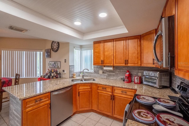 kitchen with appliances with stainless steel finishes, kitchen peninsula, light stone countertops, and sink