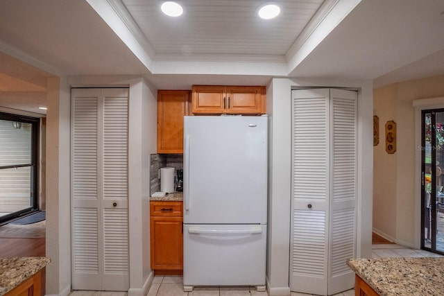 kitchen with ornamental molding, light stone counters, white fridge, and a raised ceiling