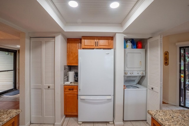 laundry area featuring ornamental molding, stacked washer / drying machine, and light tile patterned floors