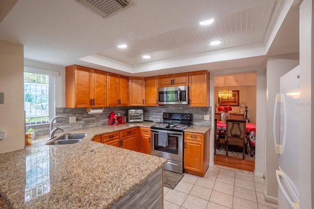 kitchen featuring stainless steel appliances, a tray ceiling, sink, light stone counters, and tasteful backsplash