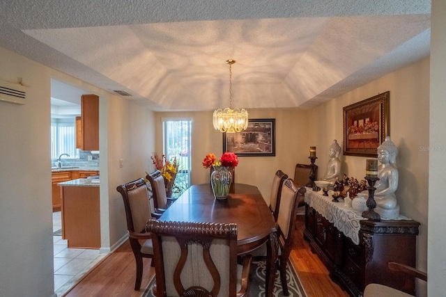 dining area with light hardwood / wood-style flooring, sink, a notable chandelier, a raised ceiling, and a textured ceiling