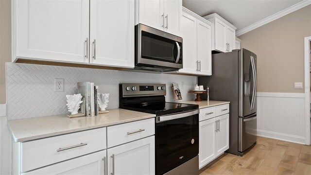 kitchen featuring white cabinets, ornamental molding, stainless steel appliances, light stone countertops, and light hardwood / wood-style floors