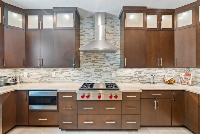 kitchen featuring wall oven, tasteful backsplash, wall chimney range hood, and stainless steel gas stovetop