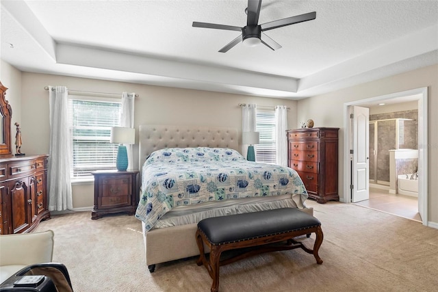 carpeted bedroom with ceiling fan, a tray ceiling, and ensuite bath