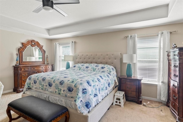 bedroom with a raised ceiling, ceiling fan, and light carpet