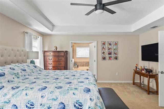 carpeted bedroom featuring a raised ceiling, connected bathroom, and ceiling fan