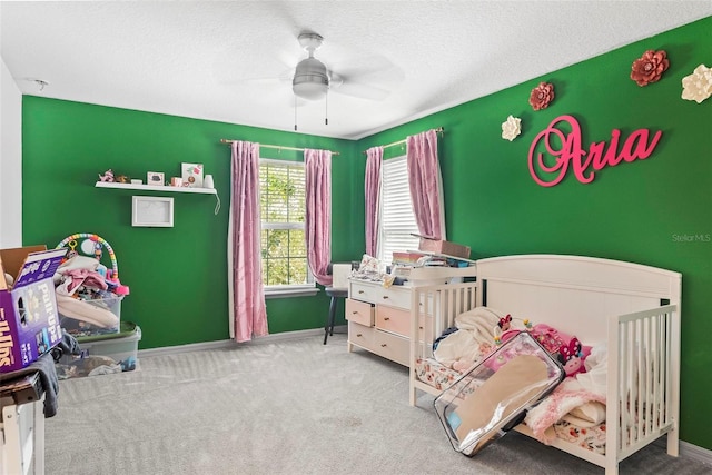 bedroom with a textured ceiling, ceiling fan, carpet floors, and a crib