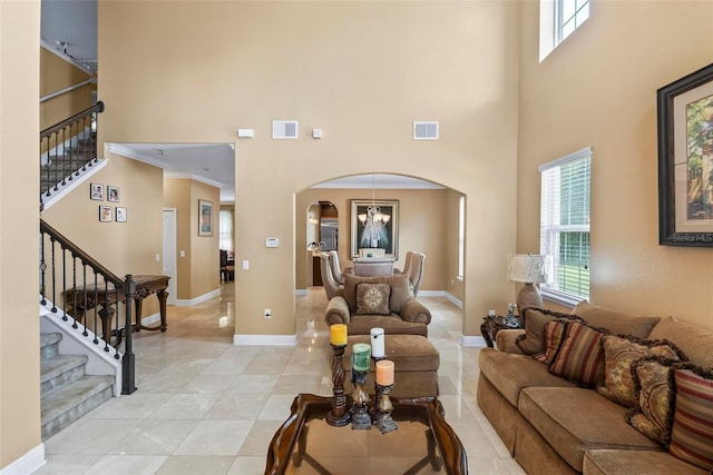 tiled living room featuring a wealth of natural light, crown molding, a towering ceiling, and a chandelier