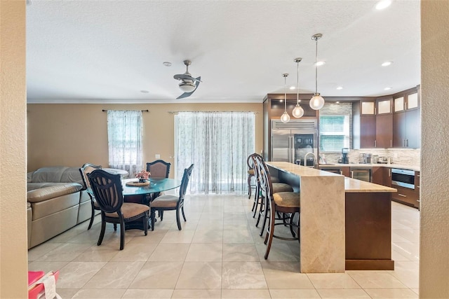 interior space with ceiling fan, built in fridge, crown molding, decorative backsplash, and a breakfast bar