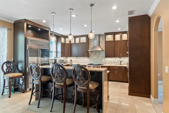 kitchen featuring dark brown cabinets, wall chimney range hood, and a center island with sink