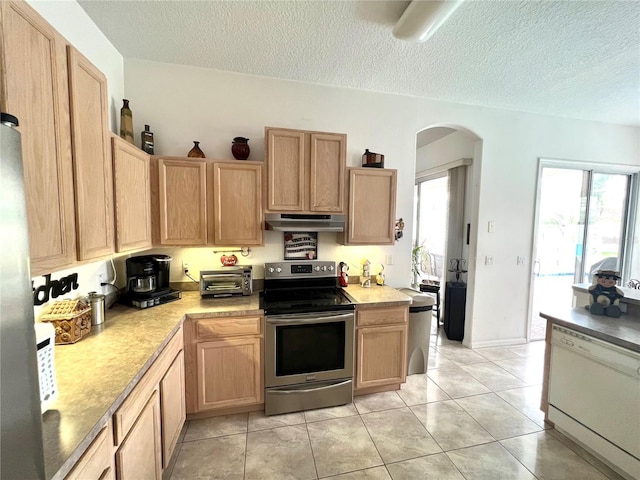 kitchen with a textured ceiling, light tile patterned flooring, light brown cabinetry, and stainless steel appliances