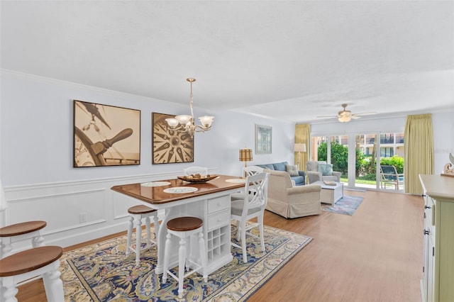 dining room with light wood-type flooring, ceiling fan with notable chandelier, and ornamental molding