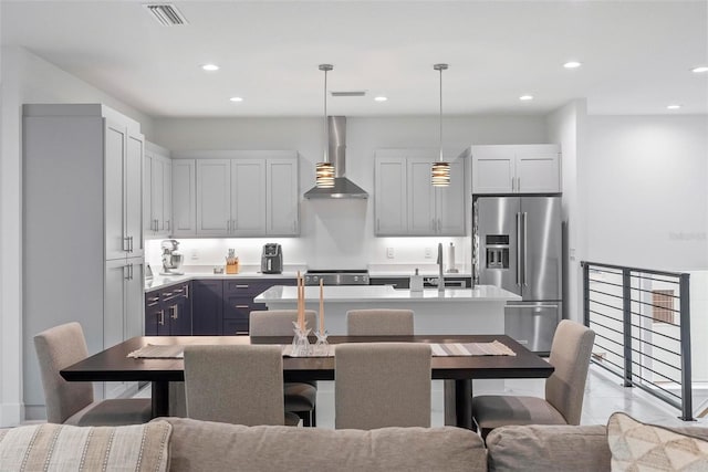 kitchen featuring hanging light fixtures, sink, a kitchen island with sink, wall chimney range hood, and appliances with stainless steel finishes