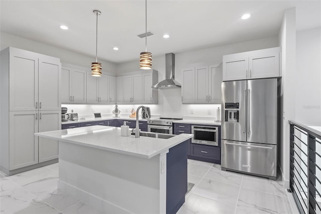 kitchen with a kitchen island with sink, hanging light fixtures, wall chimney exhaust hood, stainless steel appliances, and light stone countertops