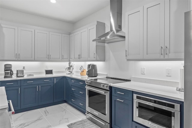 kitchen featuring blue cabinetry, wall chimney exhaust hood, stainless steel appliances, and white cabinetry