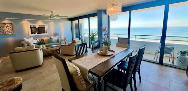 dining space with ceiling fan with notable chandelier, a healthy amount of sunlight, a water view, and a beach view